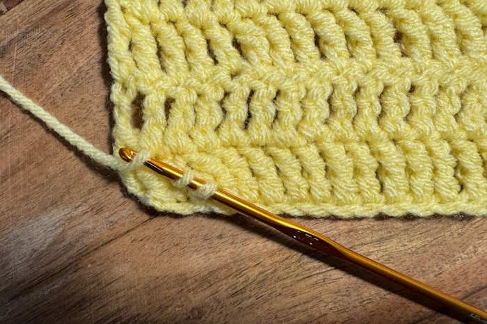 A crochet swatch of treble crochet stitch showing how to weave in ends with a crochet hook.
