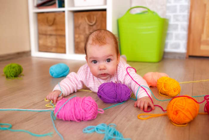 An infant is crawling on the floor with a variety of different yarn balls An infant is crawling on the floor with a variety of different yarn balls