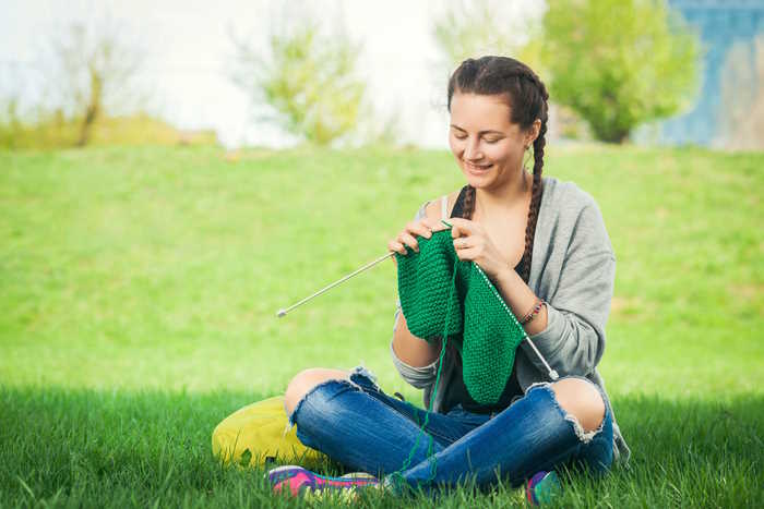 A young woman is knitting outdoors in a grassy field
