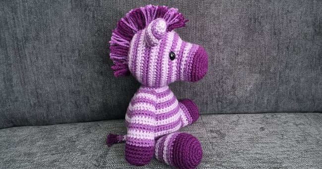 A small toy crochet zebra worked in white and purple stripes